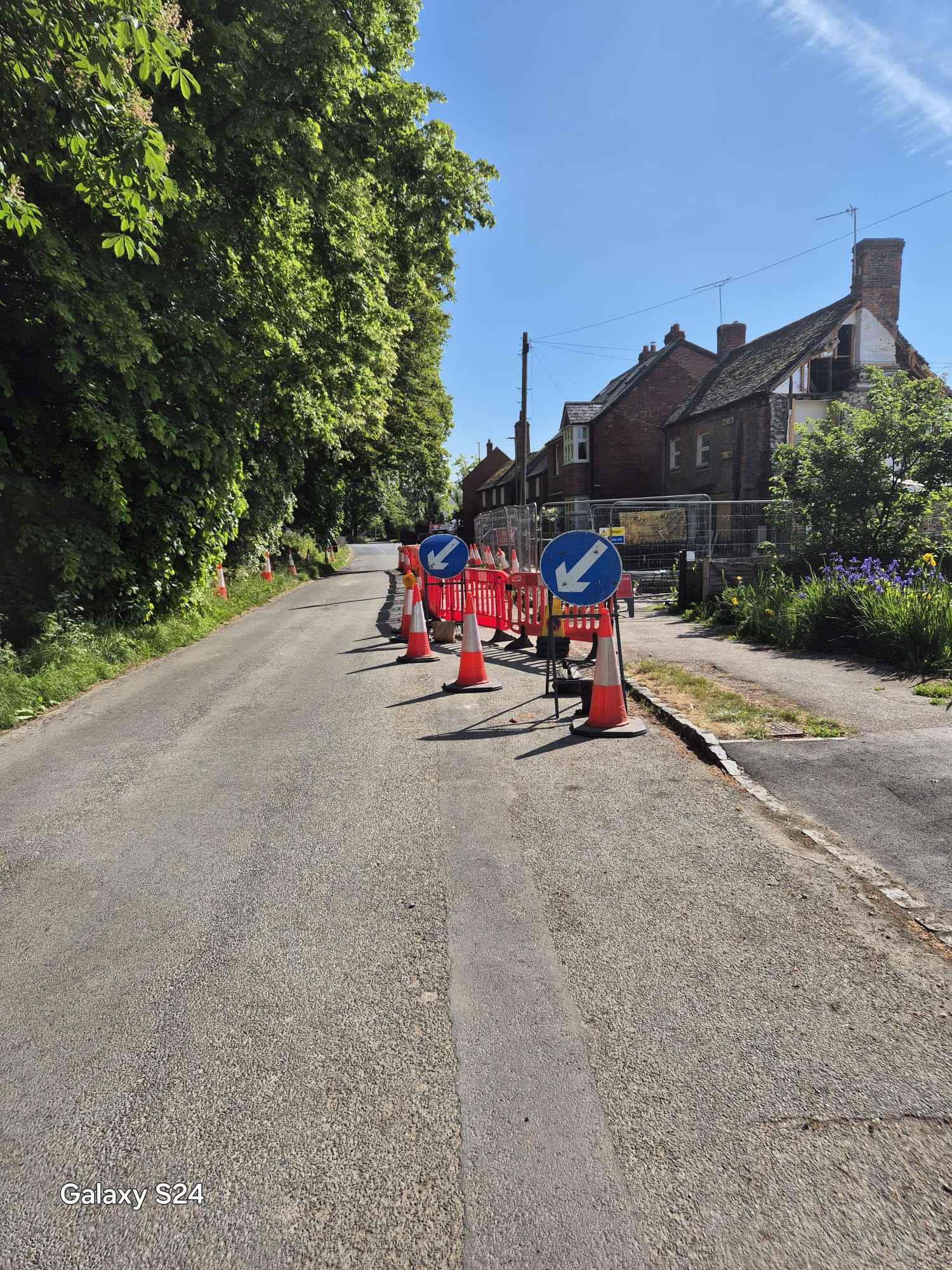 Lane narrowing with keep left signage and a long cone run guiding traffic past a village works site