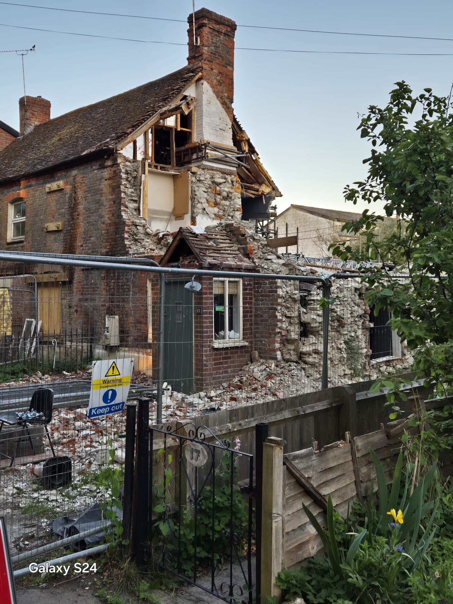Heras fencing and keep out signage protecting the public from a partially collapsed cottage in a village street