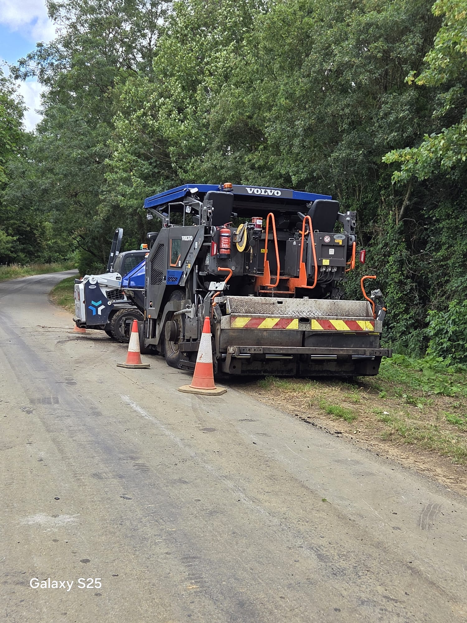 Asphalt paver and cones on a rural road resurfacing scheme managed under traffic management