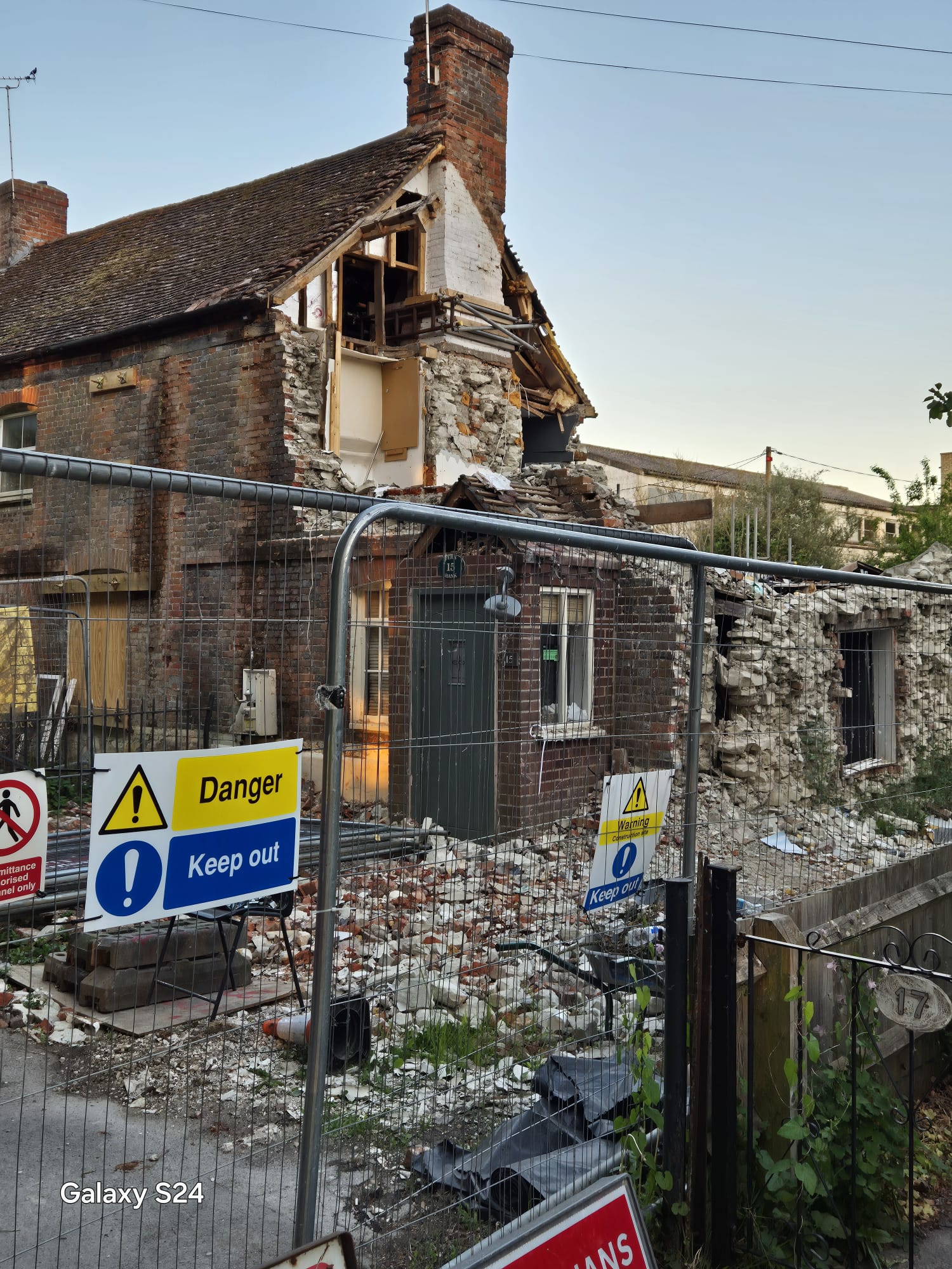 Heras fencing with danger keep out signage protecting the highway from a partially collapsed village cottage