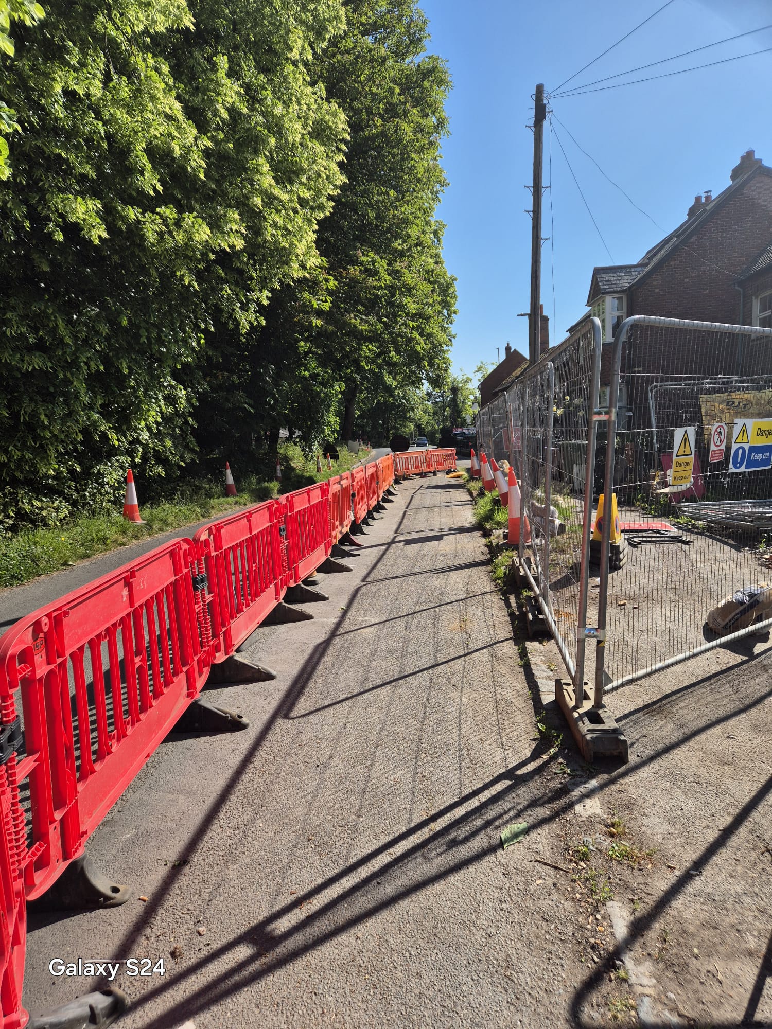 Barriered pedestrian walkway running alongside site fencing to keep people clear of works on a village road