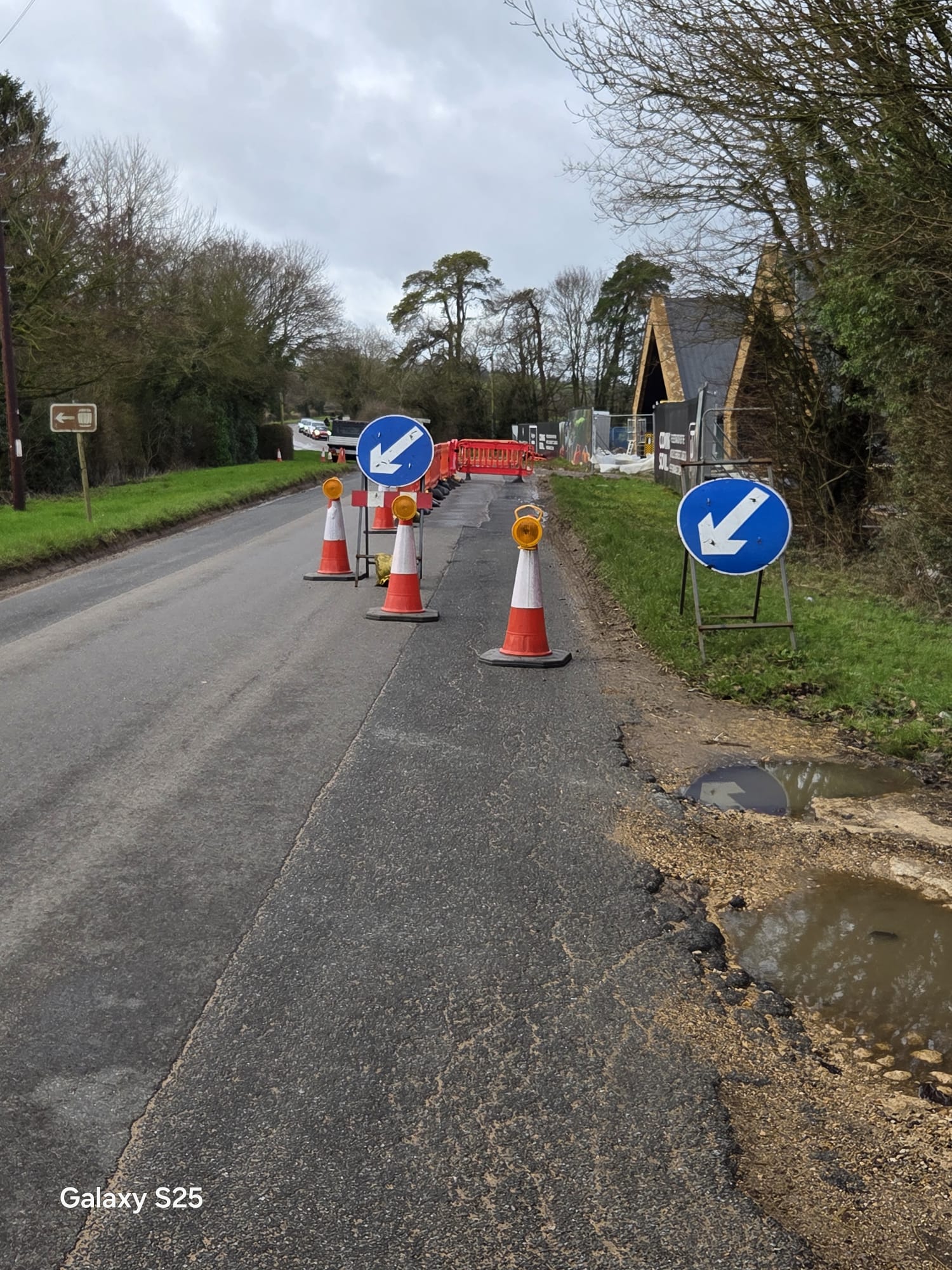 Cones and keep-left arrow signs guiding traffic past a collapsed road edge on a rural lane