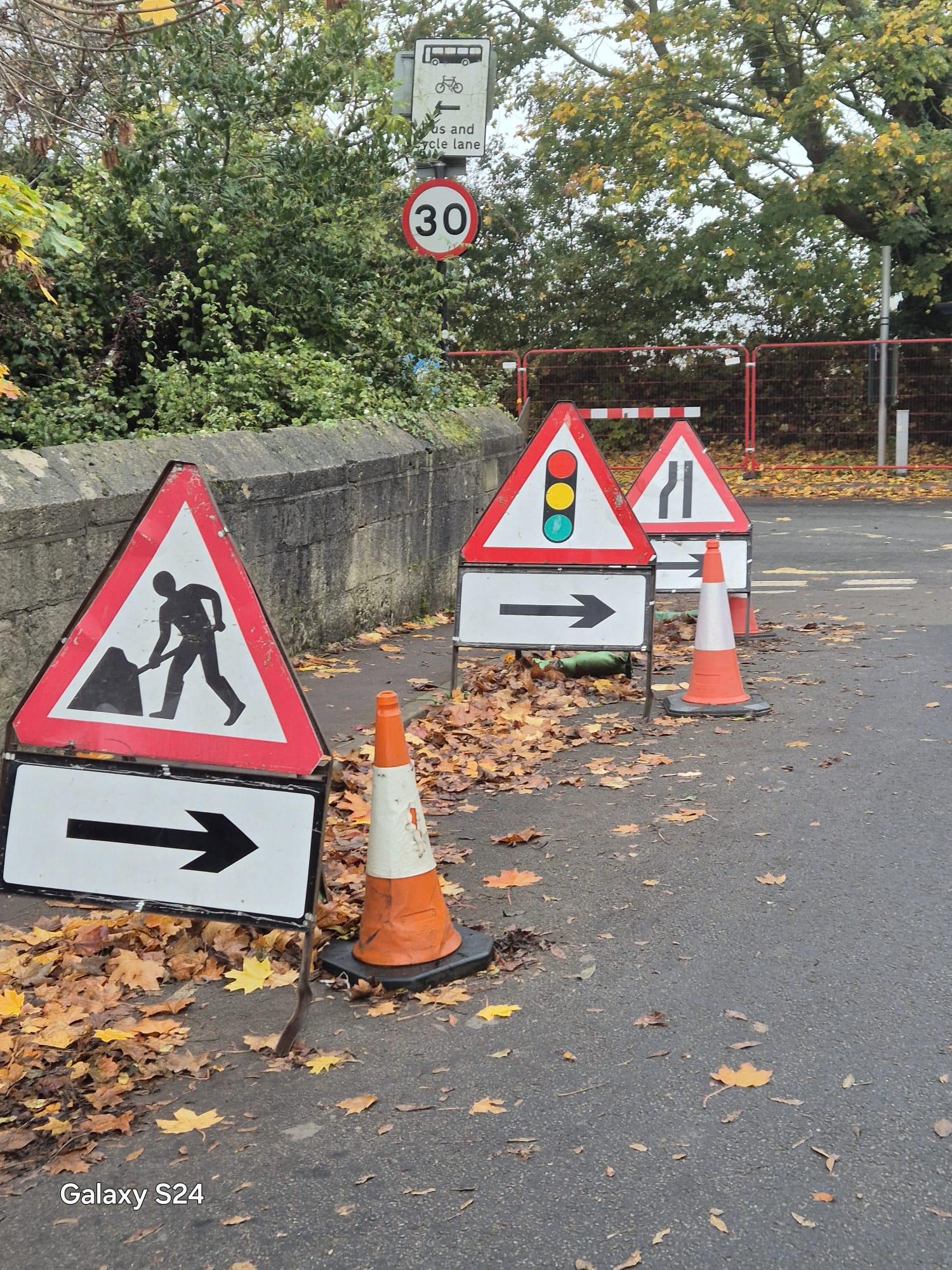 Road works, traffic signals ahead, road narrows and arrow signs set out on cones at a work site approach