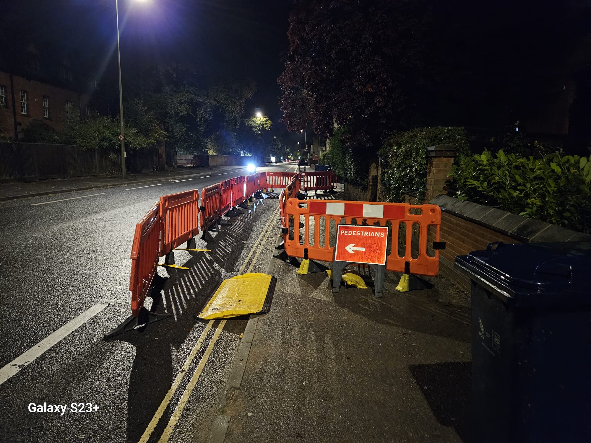 Barrier run and pedestrians arrow sign guiding people past floodlit night works alongside the kerb