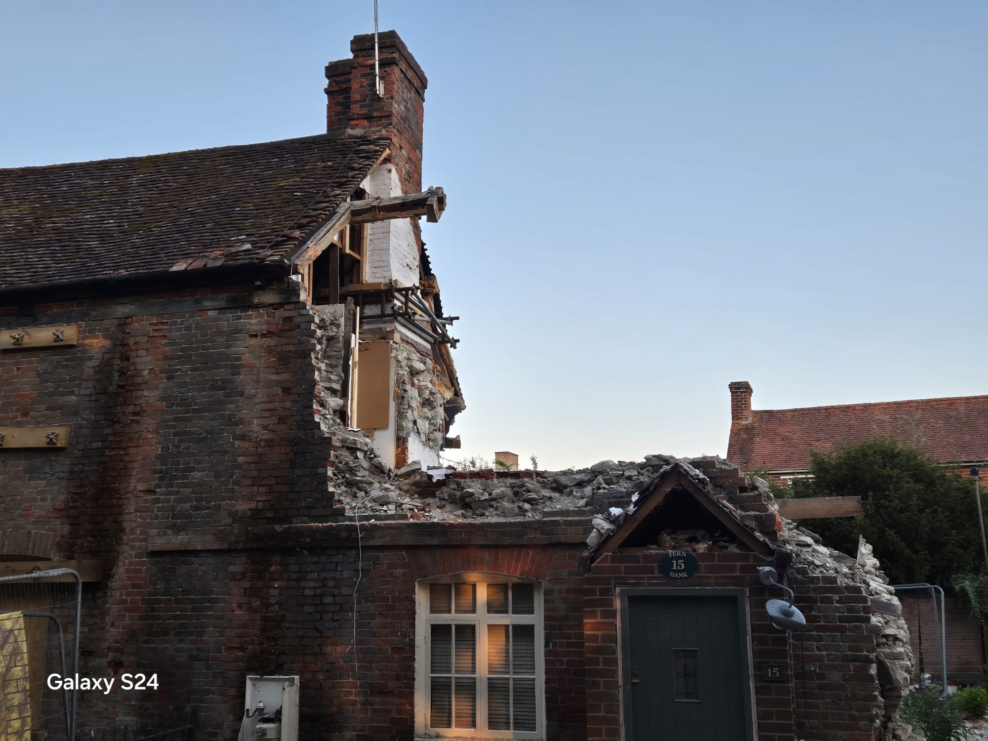 Partially collapsed brick cottage with propping and fencing installed to keep the adjacent highway safe