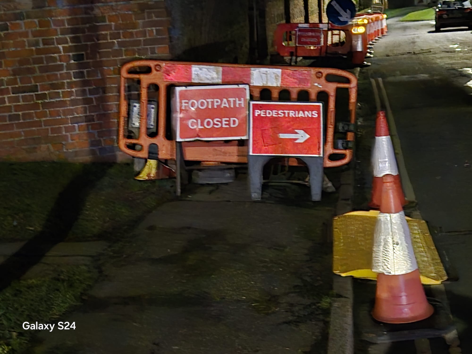 Footpath closed and pedestrian detour signage with cones at night