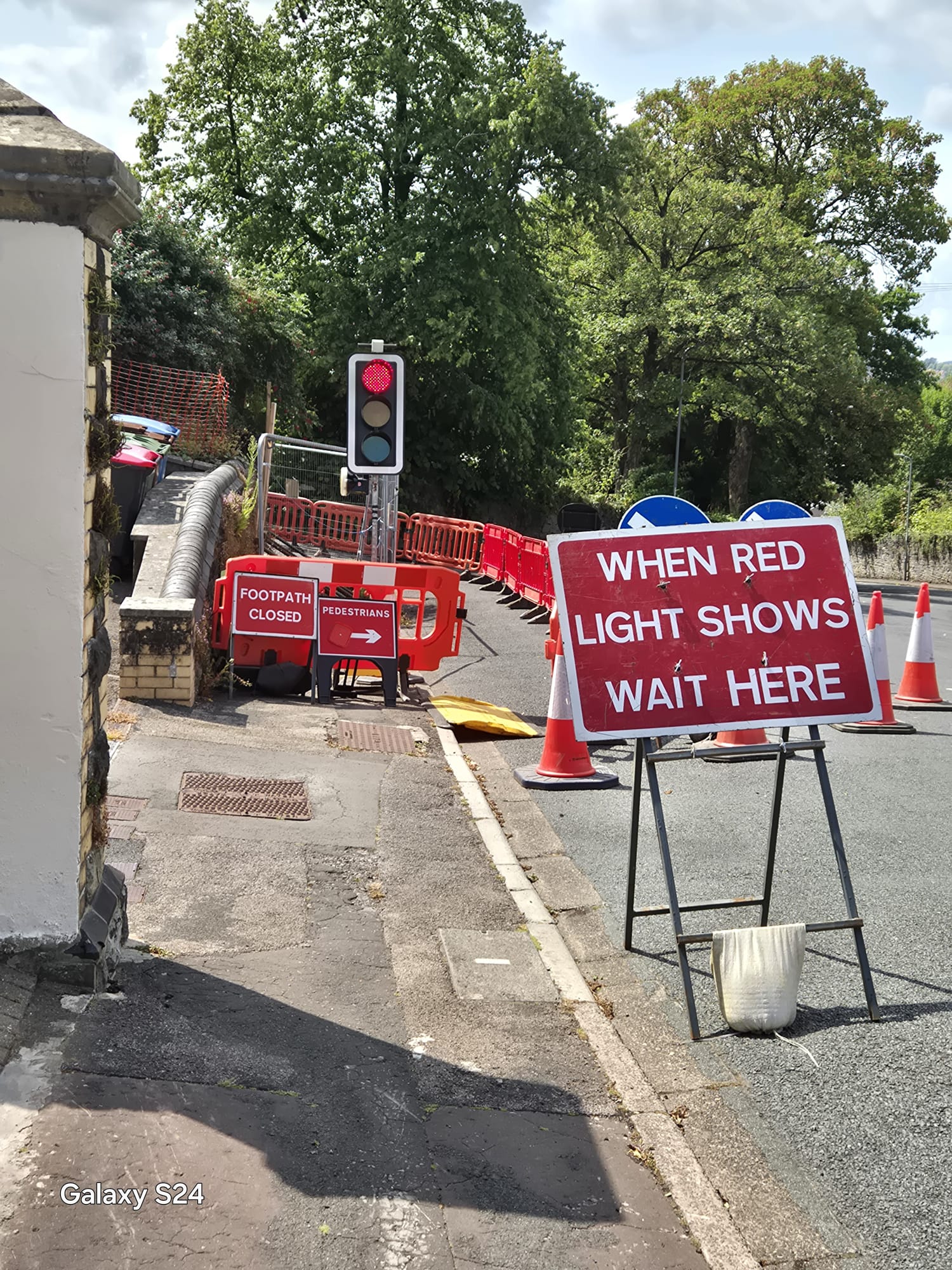Portable temporary traffic signal on red with wait here signage and a closed footway diversion