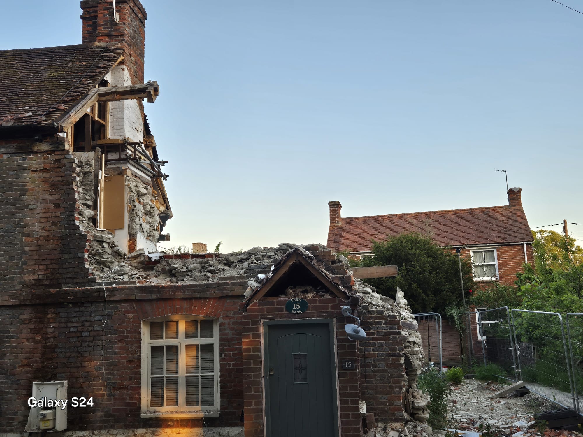 Close view of the collapsed gable and porch of a village cottage secured behind site fencing