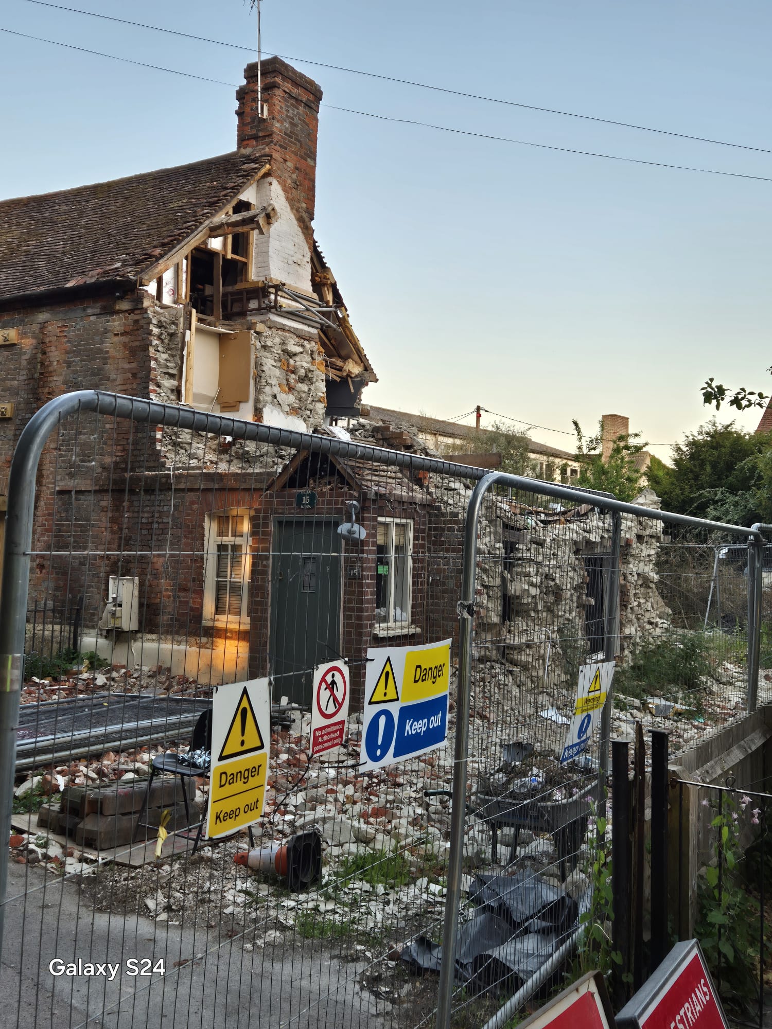 Danger keep out signage fixed to fencing around a structurally unsafe building beside a public footway