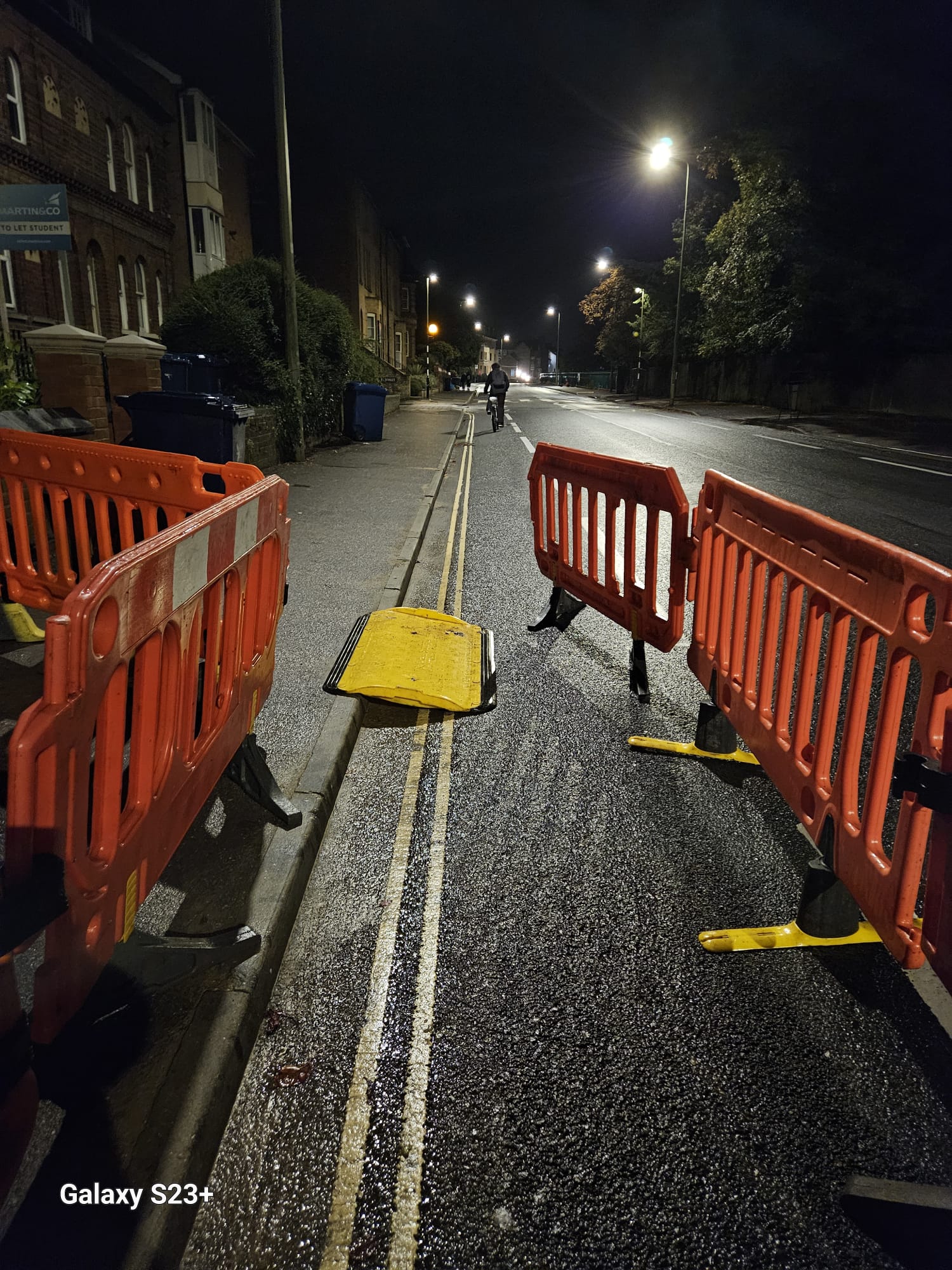 Pedestrian barriers and a cable ramp forming a protected route past night works on a residential road