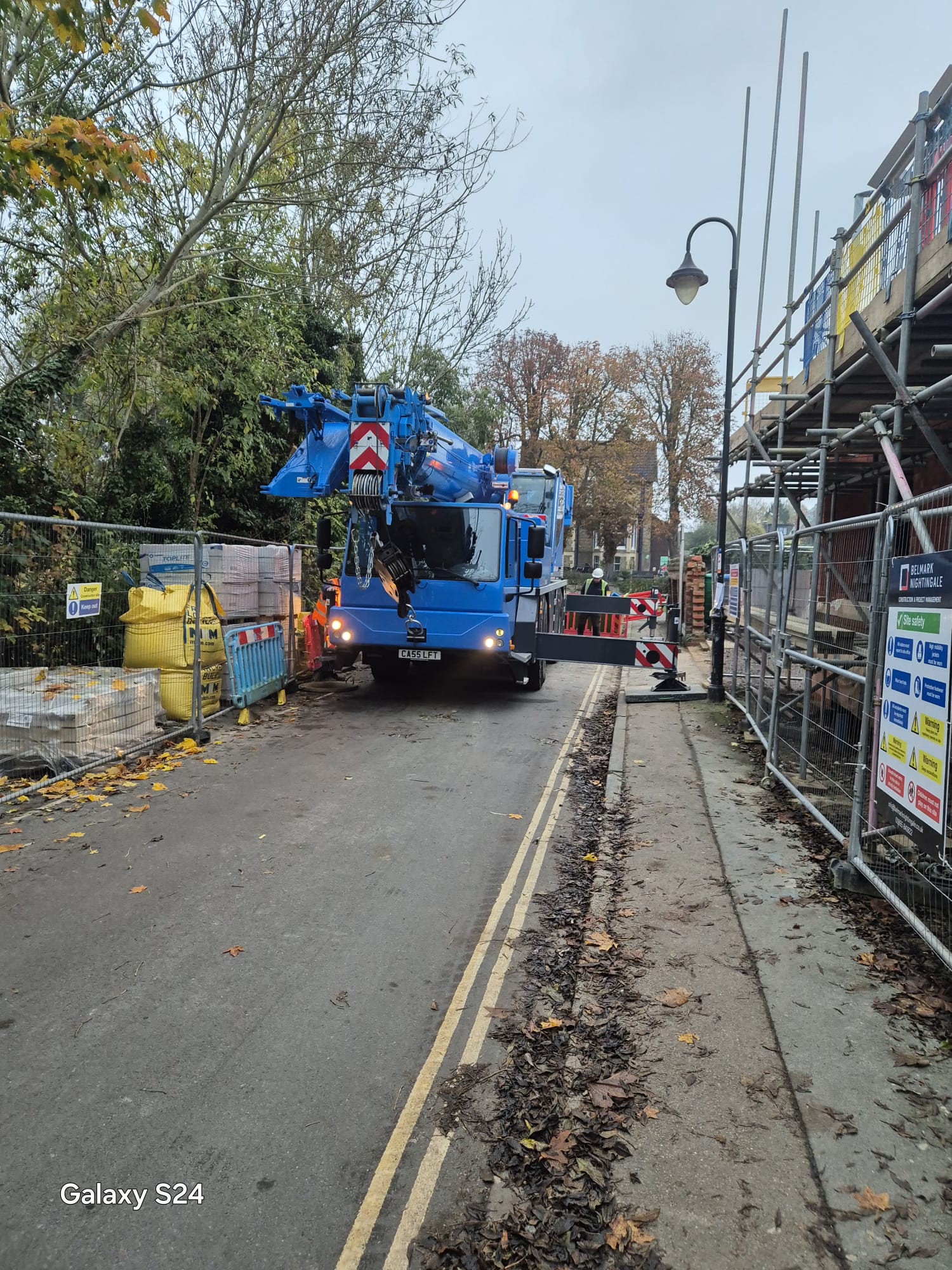 Mobile crane working in a narrow street kept clear by traffic management for a scaffolded building