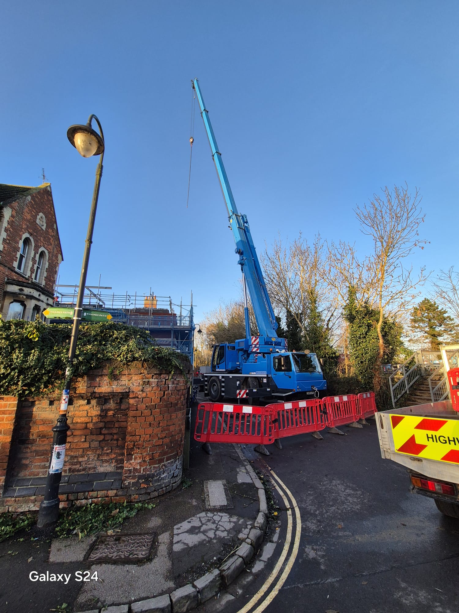Mobile crane lift on a village street protected by barriers and a highways works vehicle