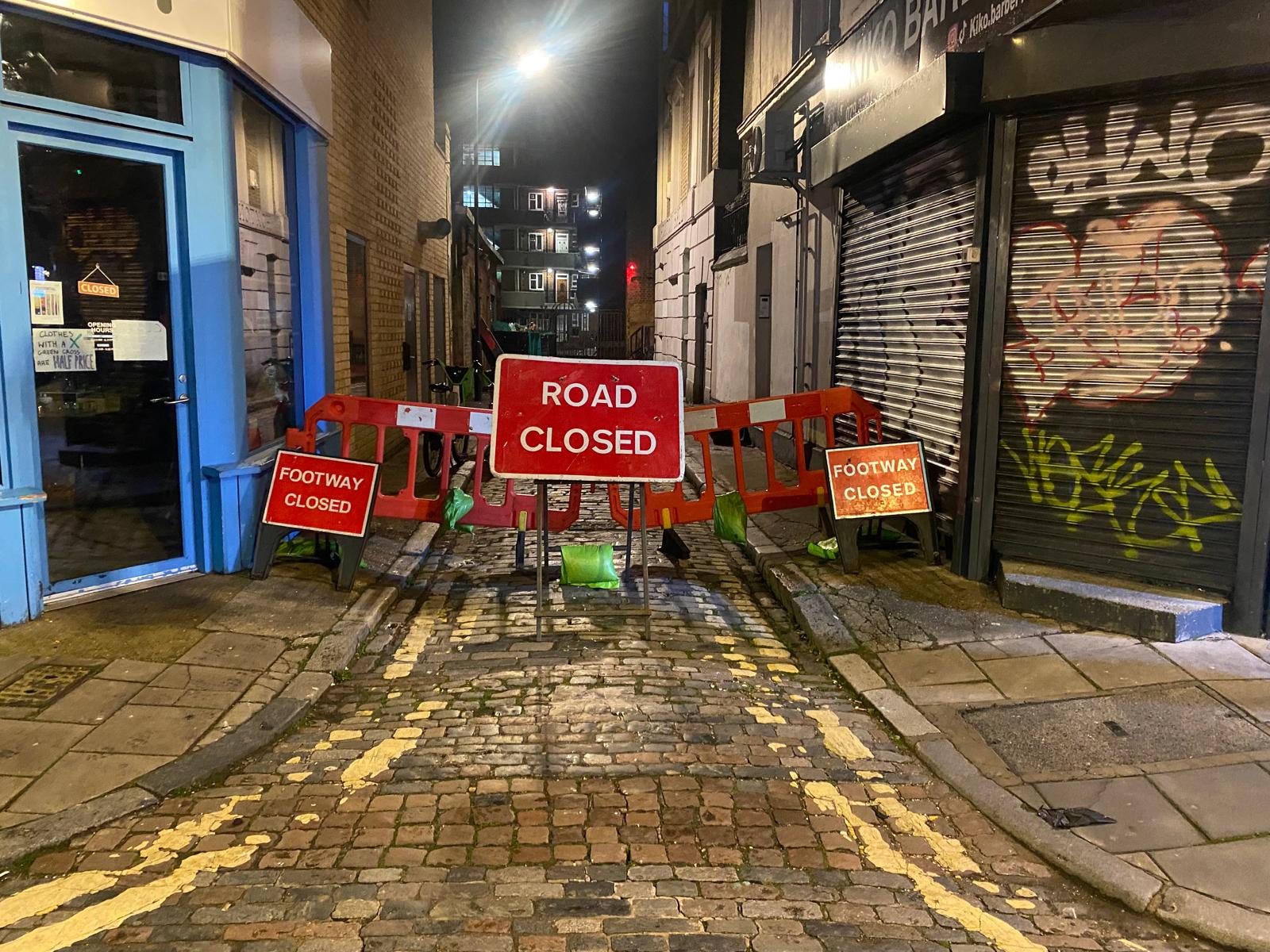 Night-time road closure blocking a narrow lane between buildings