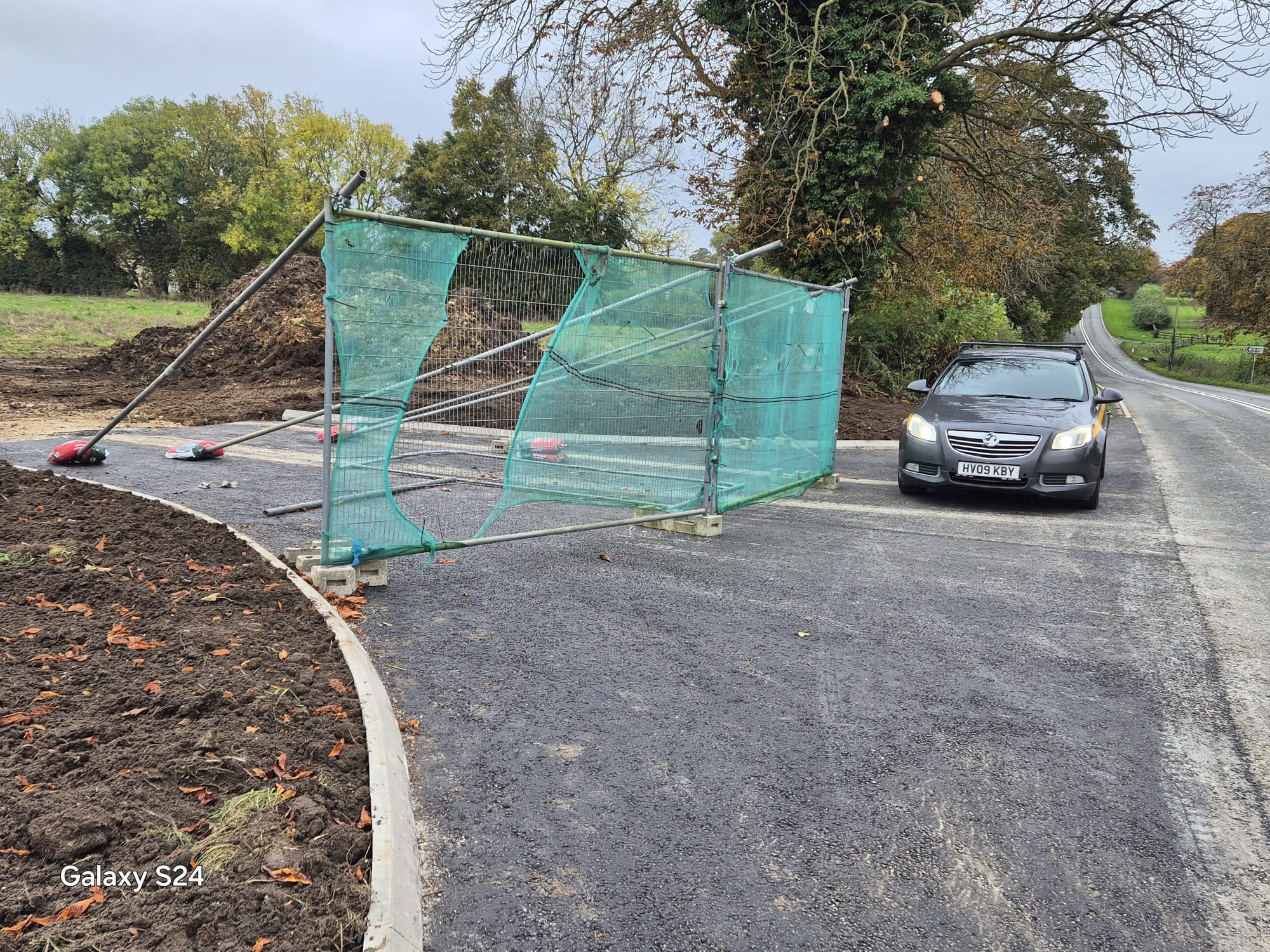 Heras fencing closing off a newly surfaced rural site access with a highway maintenance vehicle standing by on the carriageway
