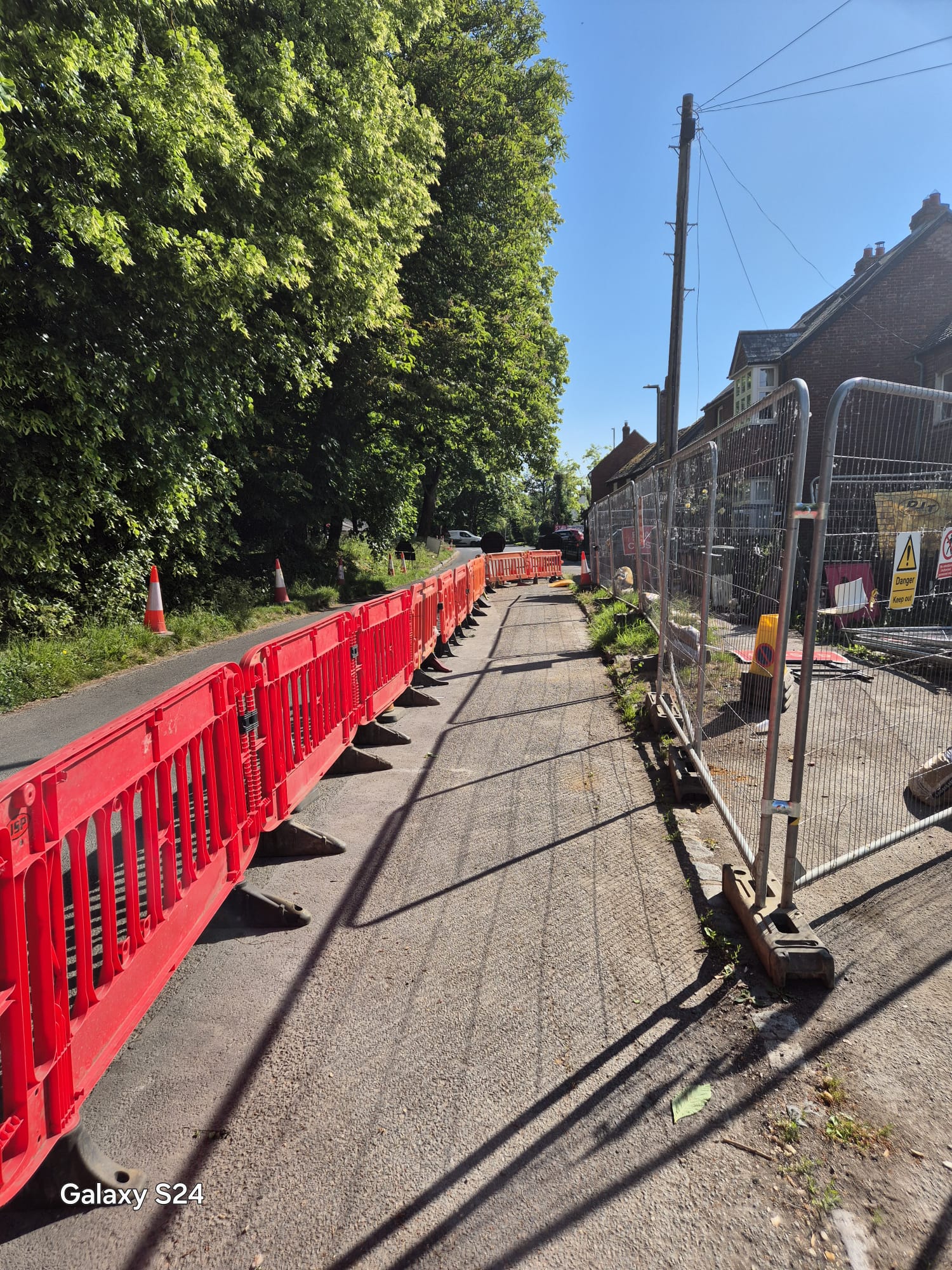 Red pedestrian barriers forming a safe walkway between site fencing and the carriageway on a village road