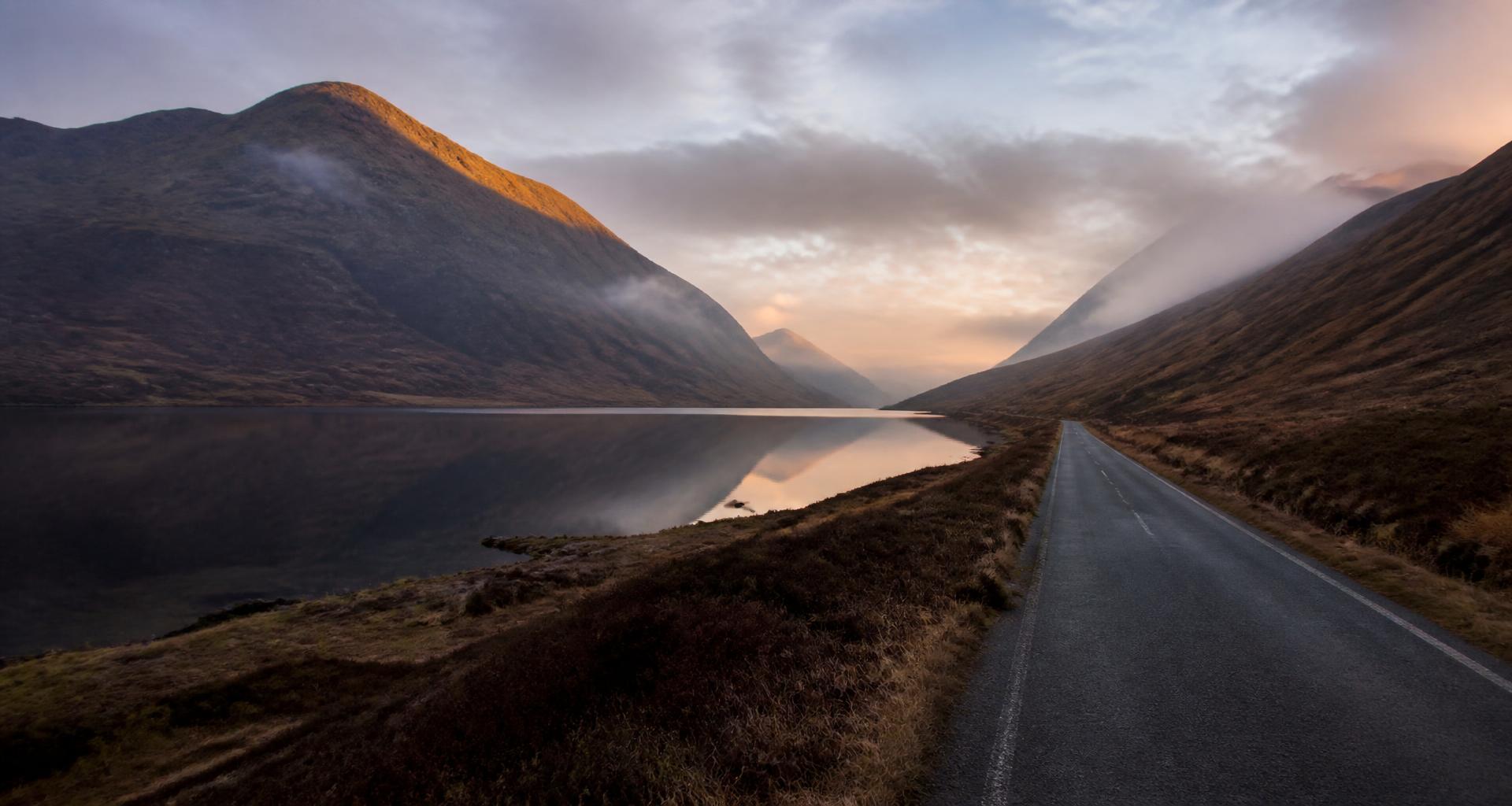 Scottish Highland road running through a glen beside a still loch at dawn