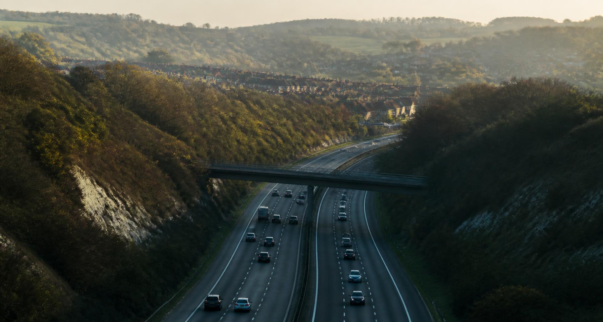 South East England dual carriageway cutting through wooded chalk downland below a commuter town